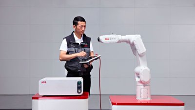 An engineer programming an ABB IRB 1200 robot arm with a tablet controller.